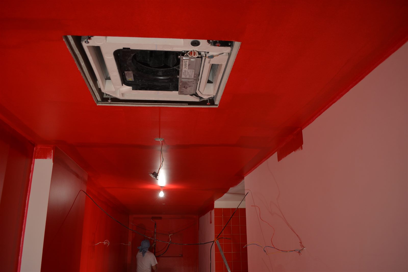 Plafond rouge en cours de finition, câbles visibles et cassette de climatisation